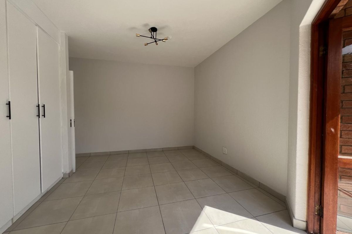 A bright, empty bedroom featuring neutral floor tiles, built-in cupboards, and a modern light fixture, offering a clean and versatile living space.