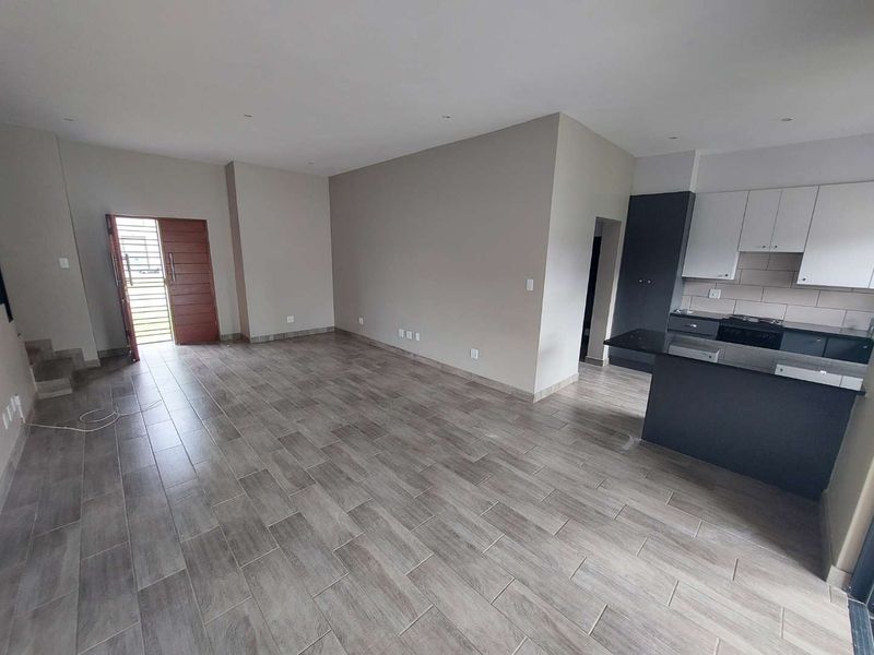 Modern open-plan living area featuring wood-look tiled flooring, recessed lighting, and a contemporary kitchen with dark cabinetry and stone countertops.