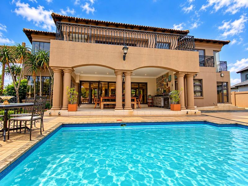 Spacious rear exterior featuring a large swimming pool, covered patio with built-in cabinetry, and an upper-level balcony with wrought iron railings.