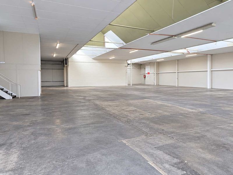 Spacious industrial warehouse featuring high ceilings with skylights, concrete flooring, and a mezzanine level, offering versatile space for various commercial or storage operations.