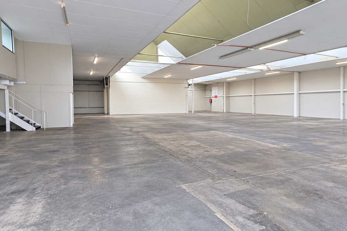 Spacious industrial warehouse featuring high ceilings with skylights, concrete flooring, and a mezzanine level, offering versatile space for various commercial or storage operations.