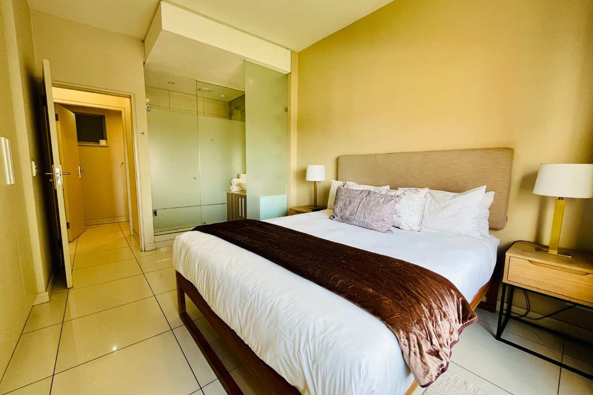 A modern bedroom featuring tiled flooring and an integrated en-suite bathroom with frosted glass partitioning.
