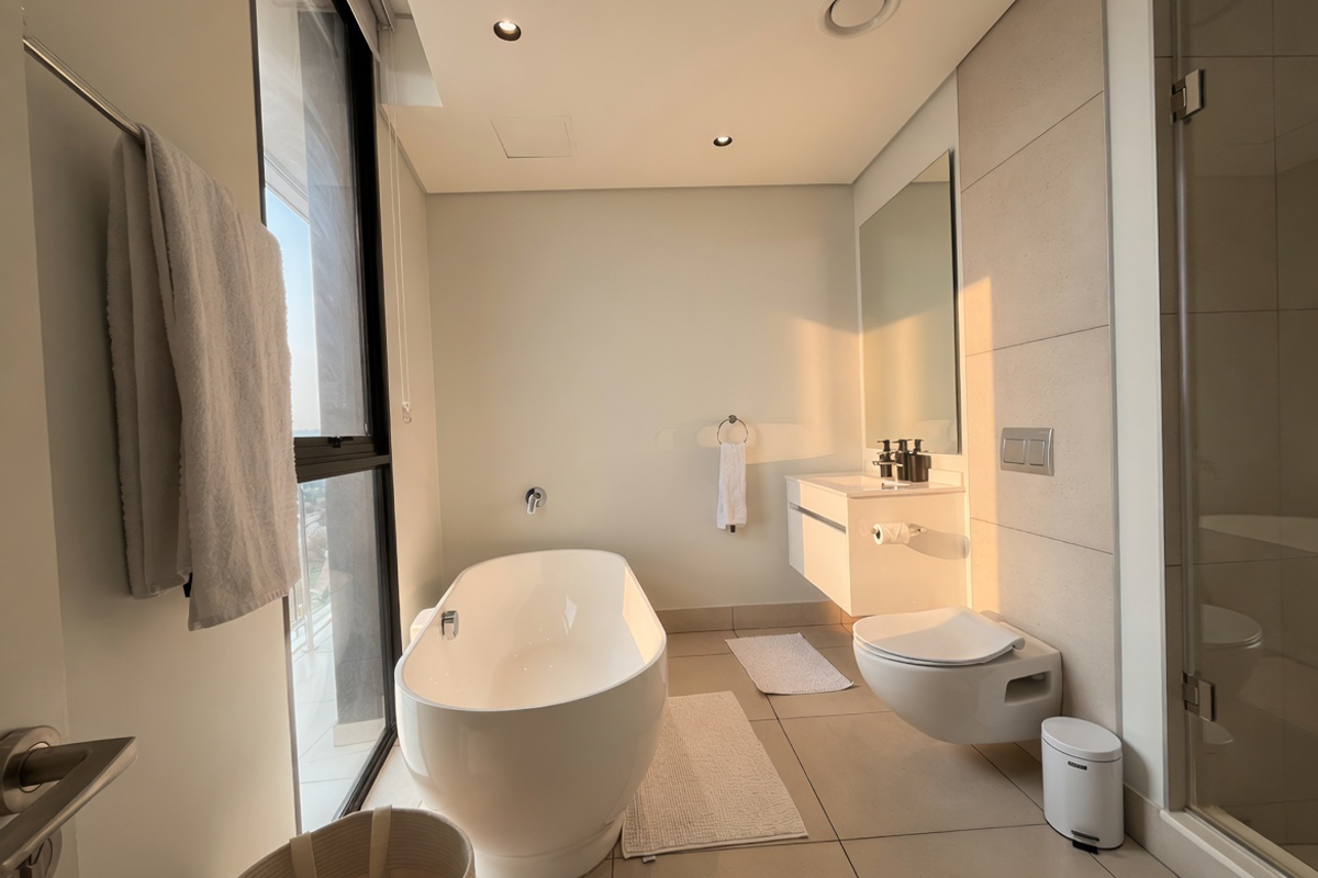 Modern bathroom featuring a sleek freestanding bathtub, wall-mounted toilet, floating vanity, and a glass-enclosed shower with neutral tile finishes.