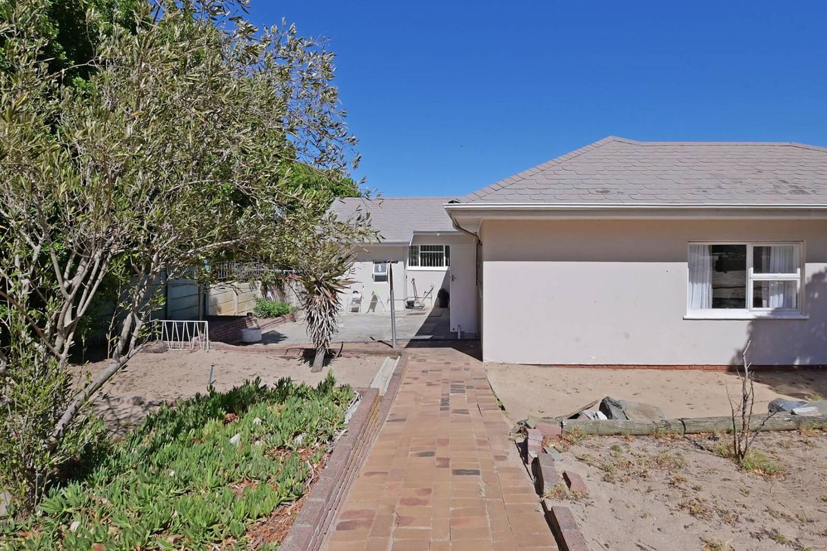 Rear view of the property featuring a paved walkway leading to the back entrance, surrounded by a garden area and established trees.