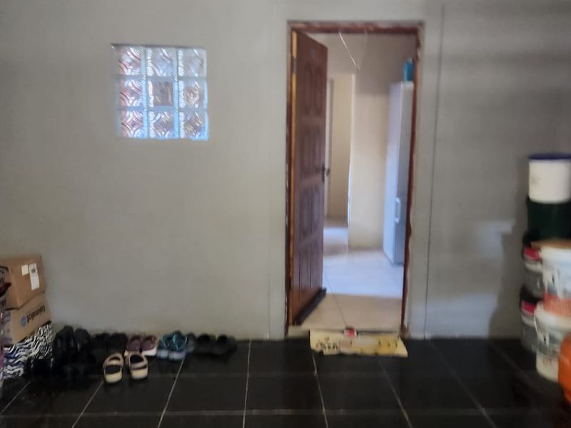An unfinished utility space featuring dark tiled flooring, a glass block window, and exposed ceiling joists with visible wiring.