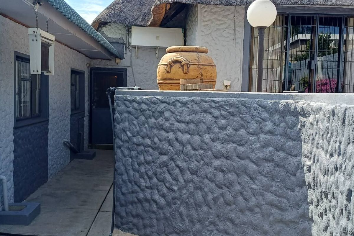 Exterior view of a property featuring a textured wall, a pathway leading to an entrance, and a traditional thatched roof section.