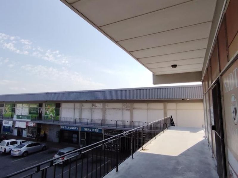 An elevated exterior walkway or balcony area featuring a metal safety railing, concrete flooring, and a protective roof canopy overlooking the parking area.