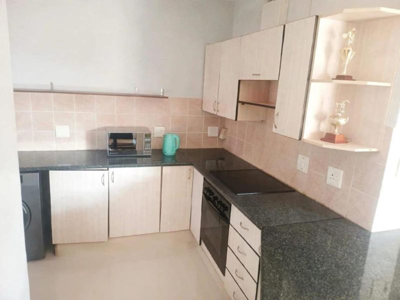 A functional kitchen featuring granite countertops, light-toned laminate cabinetry, a built-in oven with an electric hob, and a tiled backsplash.