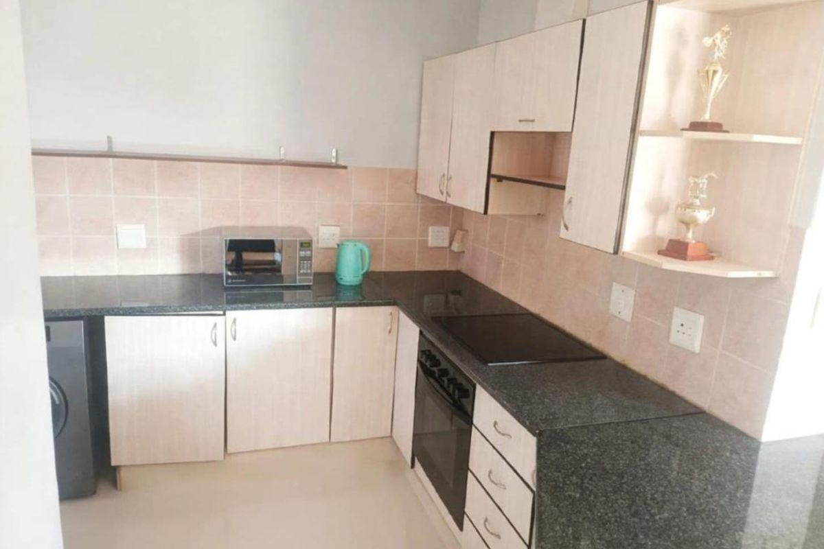 A functional kitchen featuring granite countertops, light-toned laminate cabinetry, a built-in oven with an electric hob, and a tiled backsplash.