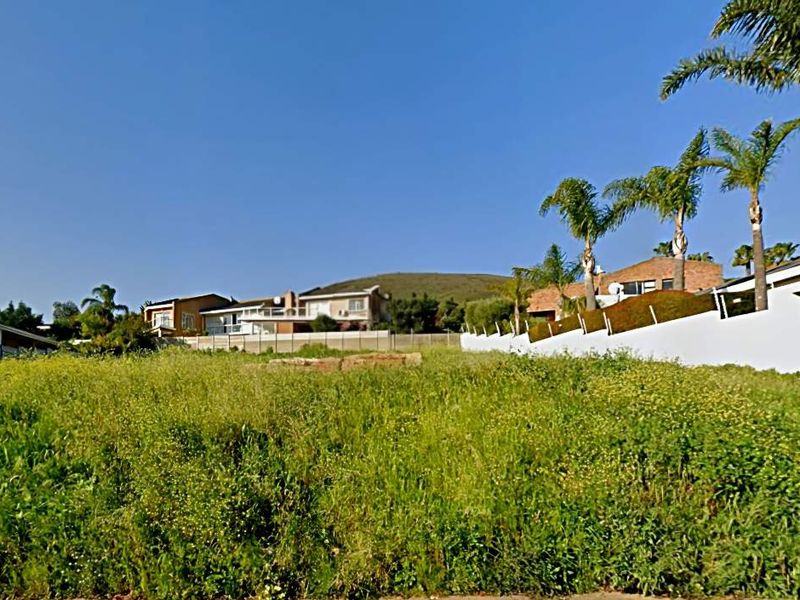 A vacant residential plot featuring natural vegetation, enclosed by perimeter walls and boundary fencing in an established neighborhood.