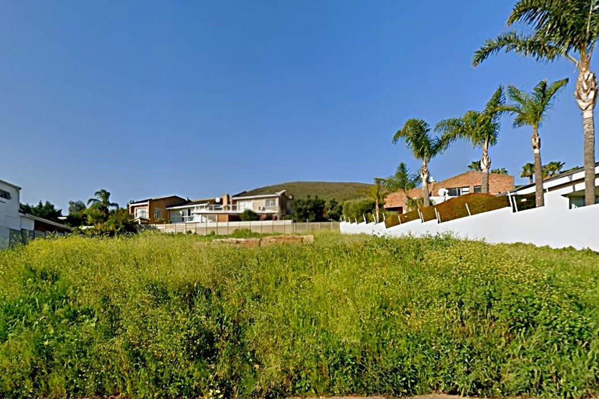 A vacant residential plot featuring natural vegetation, enclosed by perimeter walls and boundary fencing in an established neighborhood.