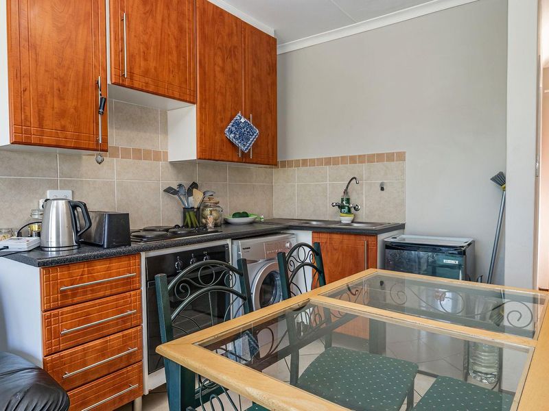 Compact kitchen featuring wood-finish cabinetry, tiled backsplash, built-in oven and hob, and tiled flooring, providing a functional workspace.