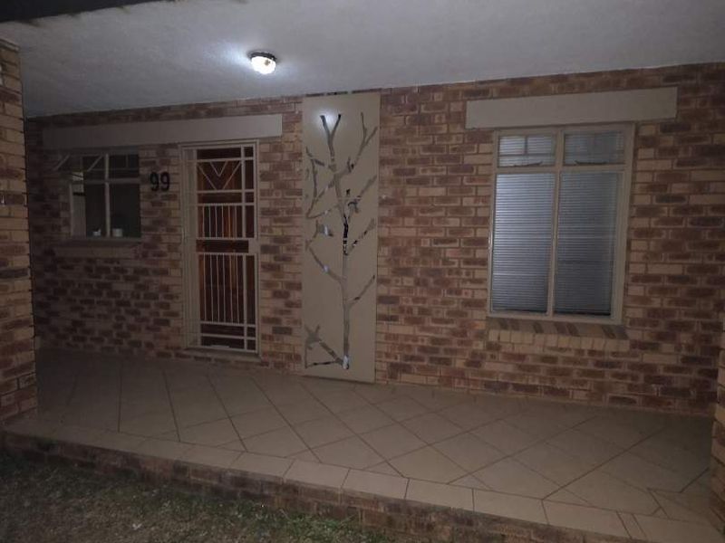 Front entrance of the apartment featuring a brick facade, tiled patio area, and secure metal gate access.