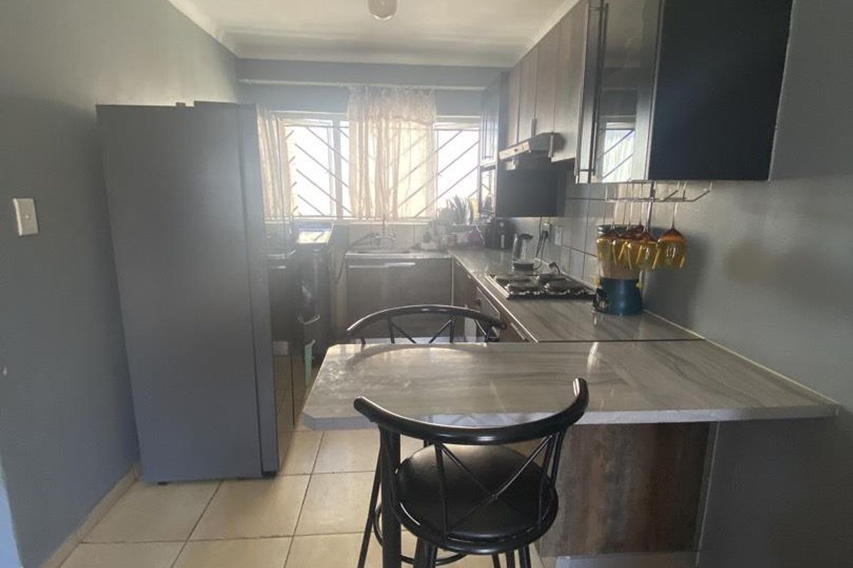 A functional kitchen featuring built-in cabinetry, a breakfast bar, tiled flooring, and a stainless steel sink with security bars on the window.