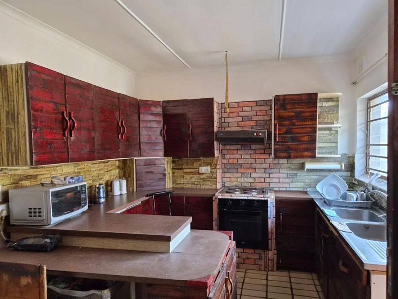 Kitchen featuring custom dark wood cabinetry, brick-style wall cladding, built-in oven and hob, and a double stainless steel sink.