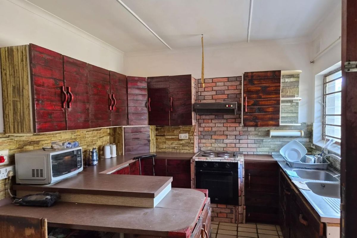 Kitchen featuring custom dark wood cabinetry, brick-style wall cladding, built-in oven and hob, and a double stainless steel sink.