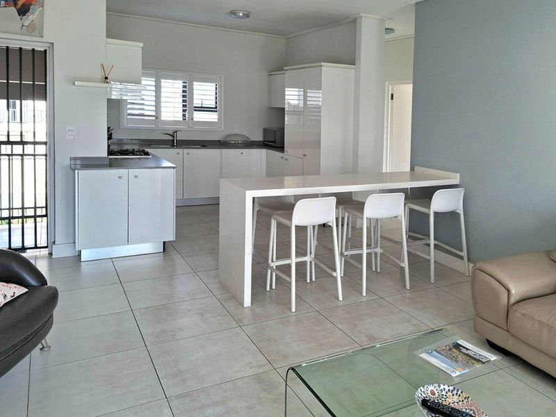 Open-plan kitchen and living area featuring modern white cabinetry, stone breakfast bar, gas hob, and neutral tiled flooring throughout.