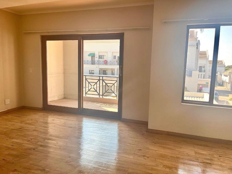 Bright and spacious living area featuring laminate flooring, large sliding doors leading to a private balcony, and ample natural light.