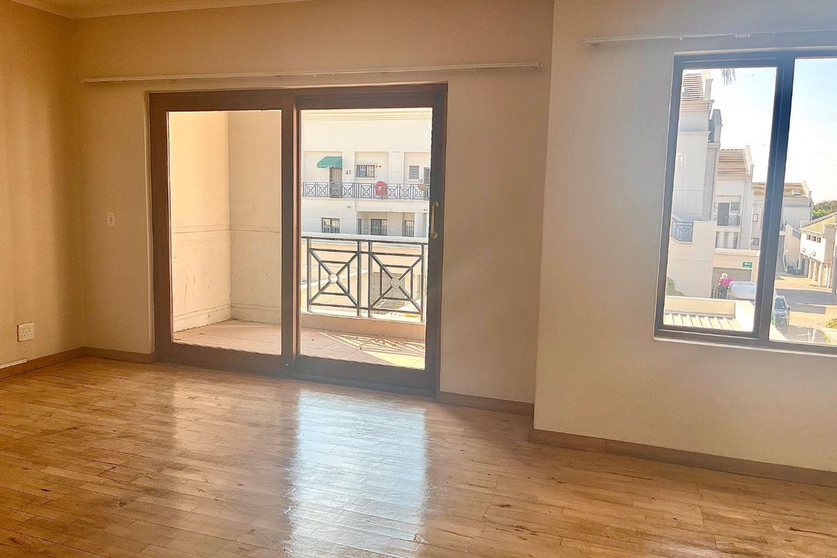 Bright and spacious living area featuring laminate flooring, large sliding doors leading to a private balcony, and ample natural light.