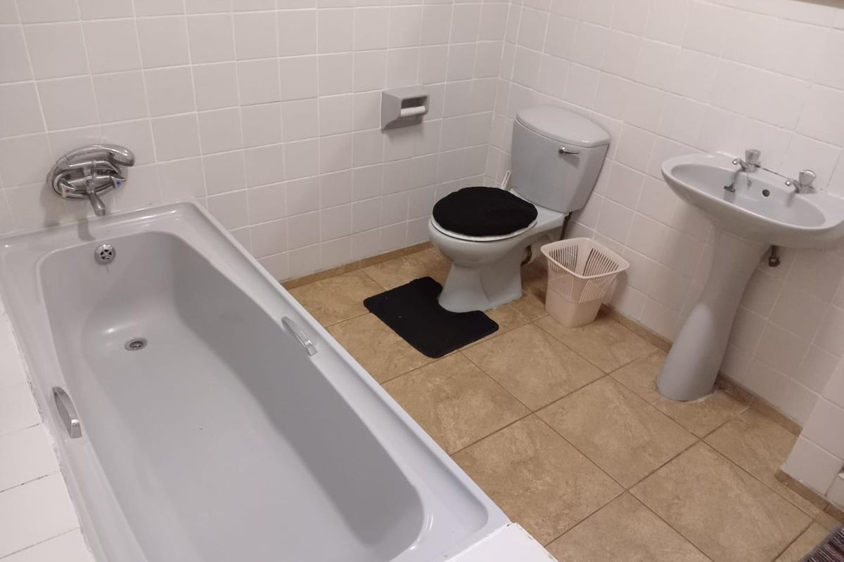A functional bathroom featuring a standard bathtub, pedestal basin, and toilet with white wall tiling and neutral floor tiles.