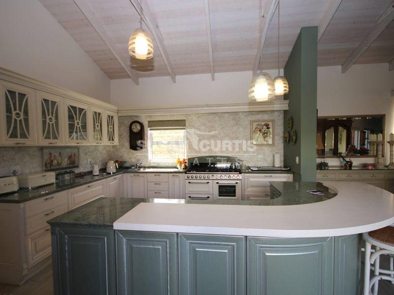 Spacious kitchen featuring custom cabinetry, stone countertops, a gas stove, and a large breakfast bar under an exposed beam ceiling.