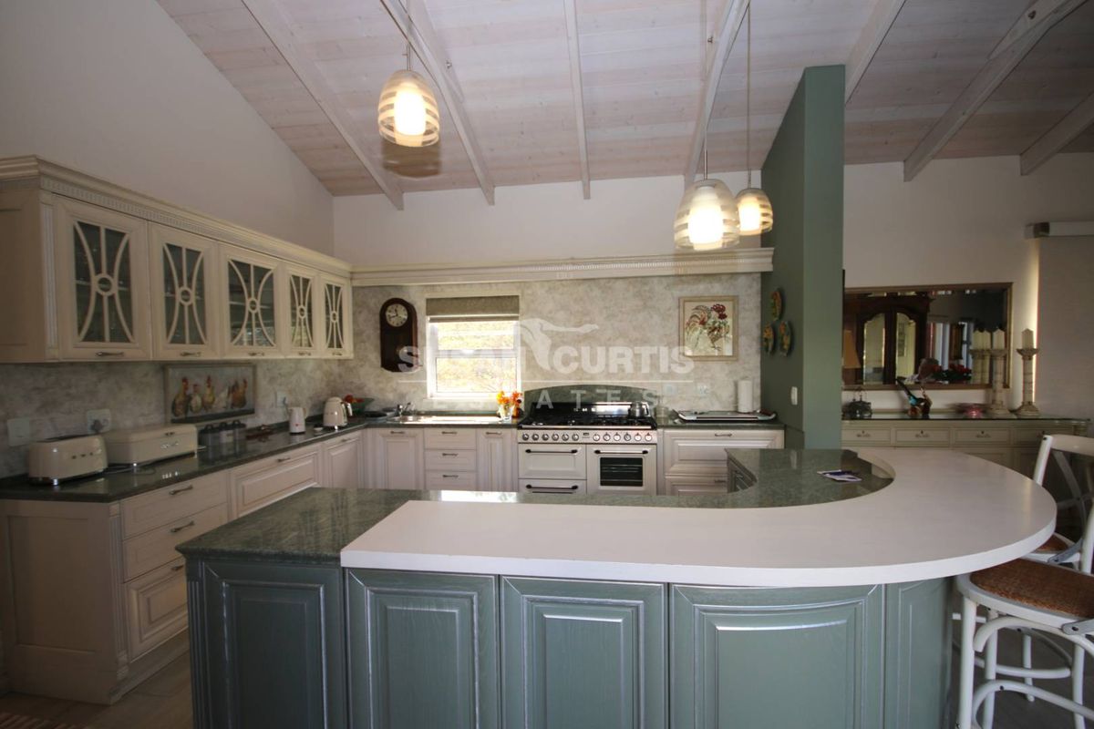 Spacious kitchen featuring custom cabinetry, stone countertops, a gas stove, and a large breakfast bar under an exposed beam ceiling.