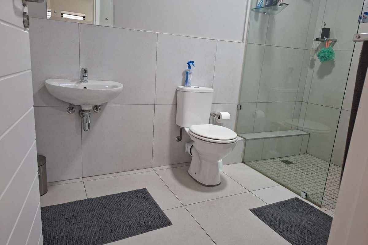 Modern bathroom featuring large format floor and wall tiles, a wall-mounted basin, a close-coupled toilet, and a glass-enclosed walk-in shower.
