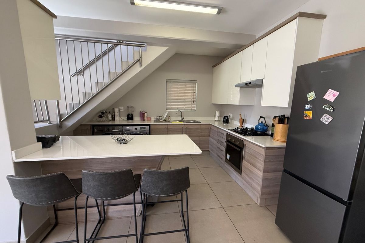 Modern kitchen featuring light wood-tone cabinetry, stone countertops, integrated appliances, and a breakfast bar, conveniently situated beneath a staircase.
