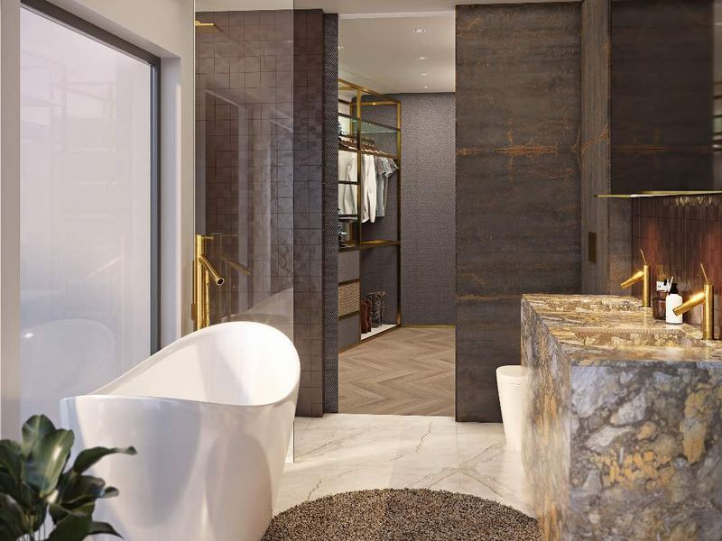 Luxurious modern bathroom featuring a freestanding bathtub, stone-topped double vanity with brass fixtures, and an integrated walk-in closet with high-end finishes.