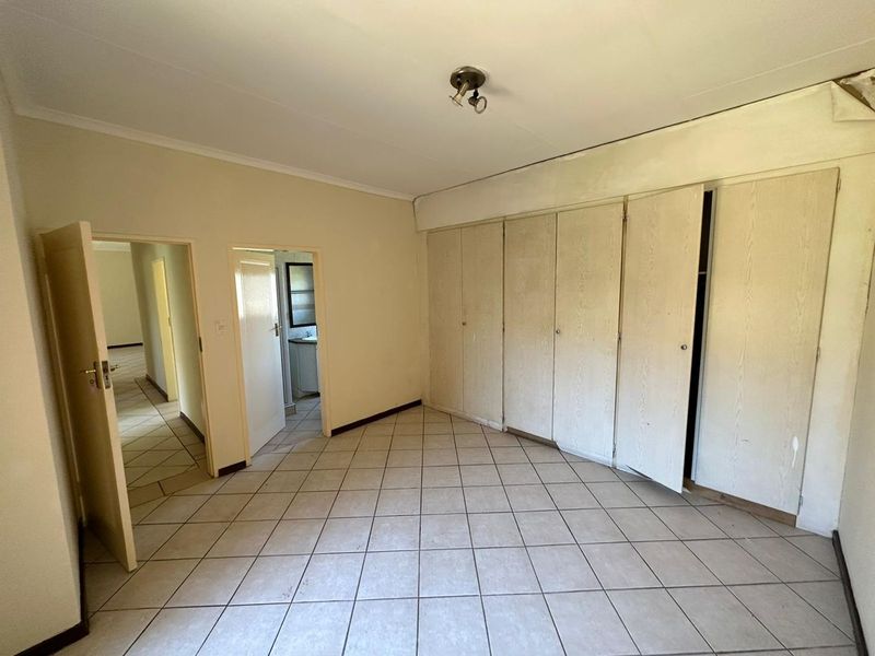 An empty bedroom featuring tiled flooring and extensive built-in cupboard storage, requiring cosmetic updates to the ceiling and cabinetry.