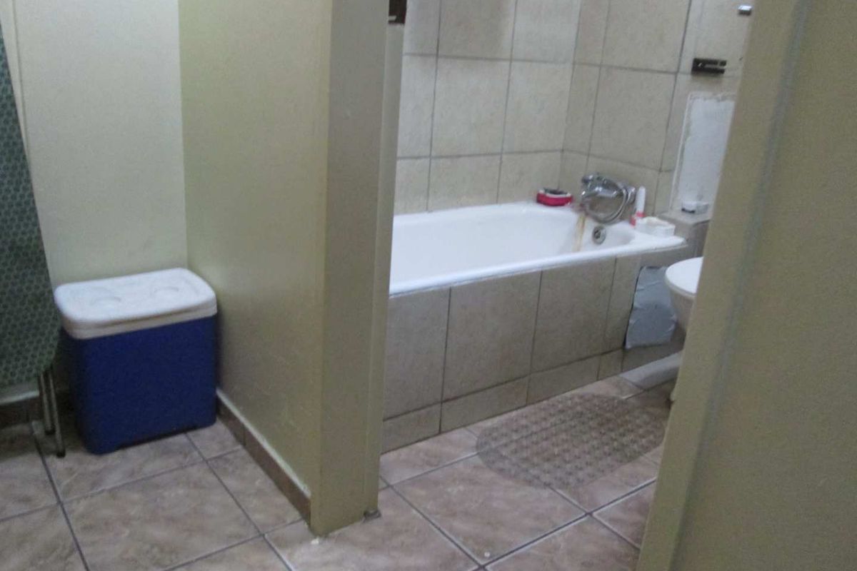 A functional bathroom featuring a tiled bathtub surround and floor, requiring some cosmetic updates to the wall finishes and general maintenance.