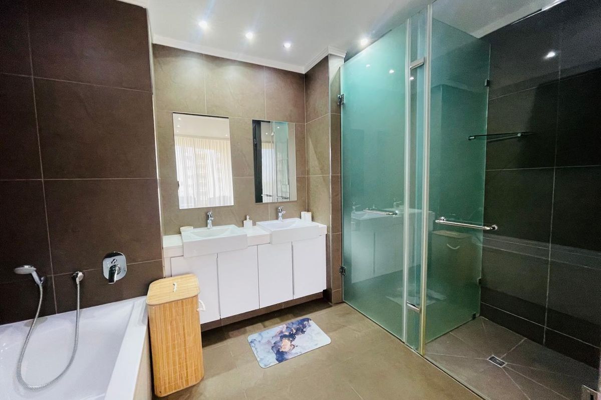 Modern bathroom featuring a double vanity with wall-mounted faucets, a spacious glass-enclosed shower, and a separate built-in bathtub with contemporary dark tiling.