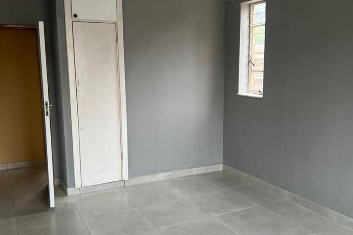 A vacant room featuring grey tiled flooring, neutral grey walls, and a built-in storage cupboard with overhead cabinet.