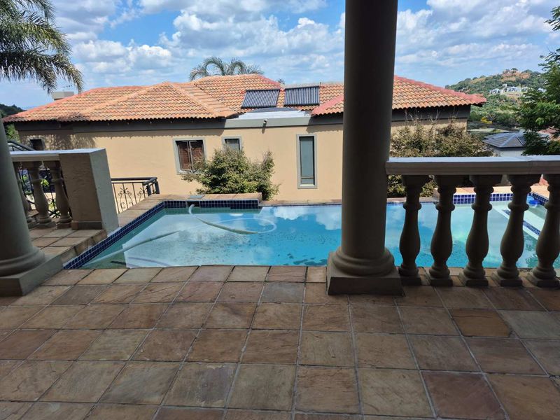 A view from a covered patio overlooking a swimming pool with stone tiling and classic balustrade detailing, set against a residential backdrop.