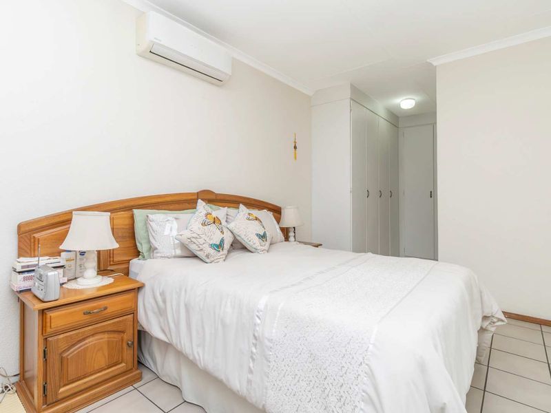 A functional bedroom featuring tiled flooring, built-in cupboards for storage, and a wall-mounted split-system air conditioning unit.