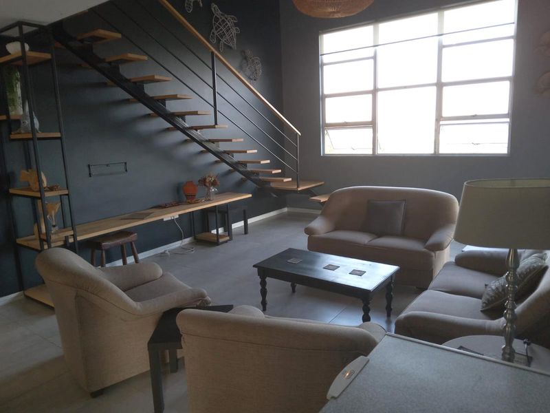 Spacious living room featuring a modern floating staircase, large windows providing ample natural light, and contemporary dark wall finishes.