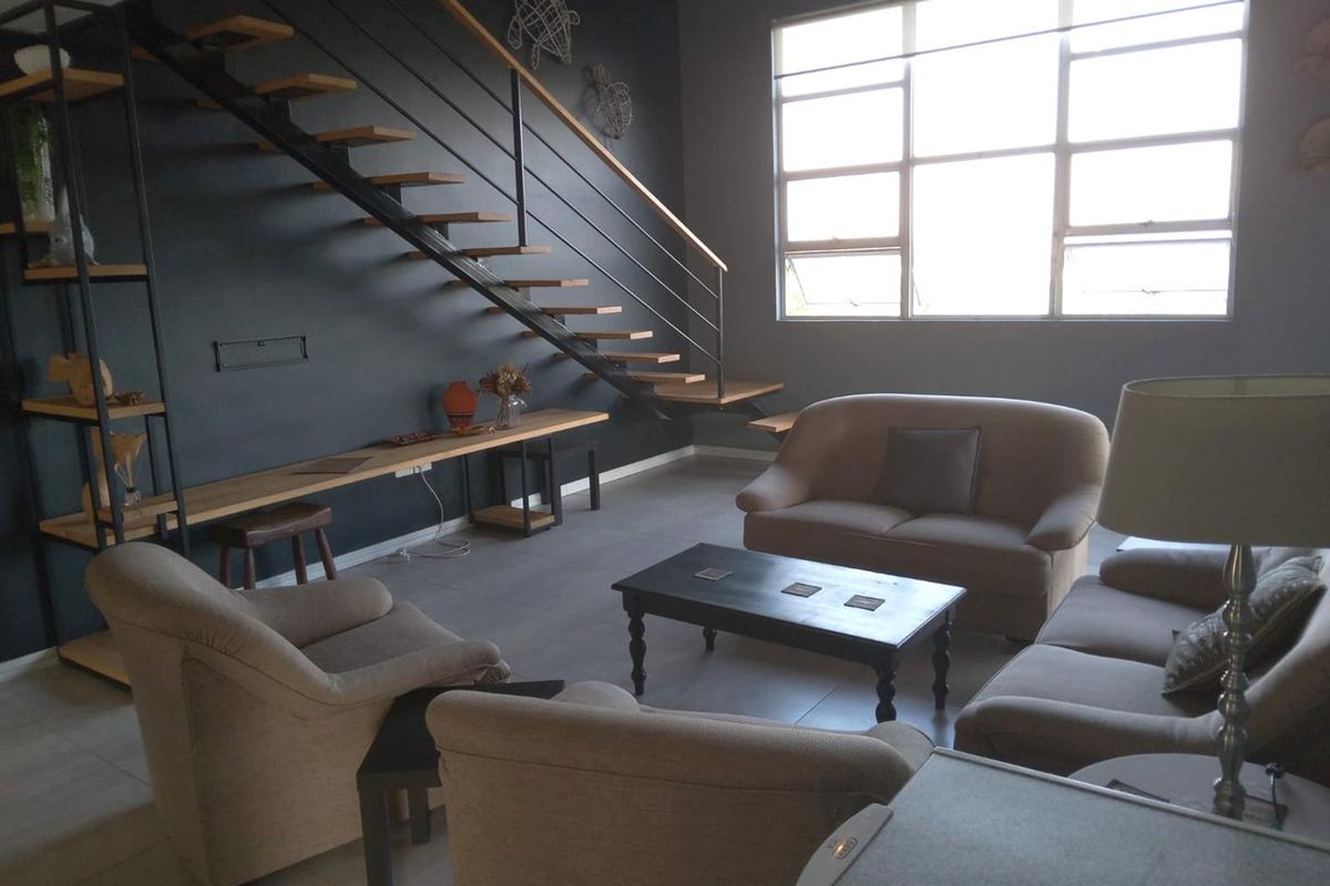 Spacious living room featuring a modern floating staircase, large windows providing ample natural light, and contemporary dark wall finishes.