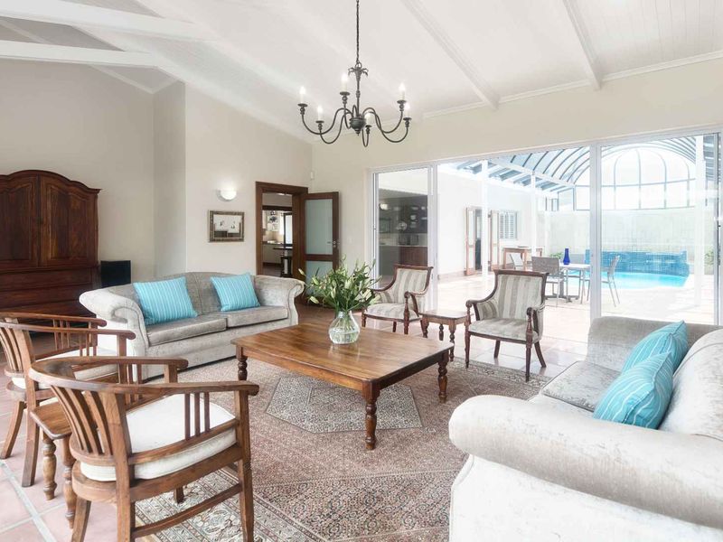 Spacious living room featuring a vaulted ceiling with exposed beams, a classic chandelier, and large sliding glass doors opening to a pool area.