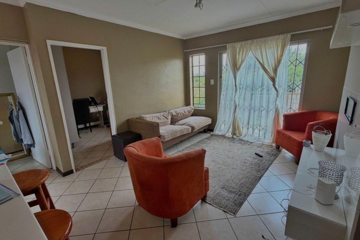 A living room featuring tiled flooring, a sliding door with security gate, and neutral wall tones, providing access to an adjacent room.