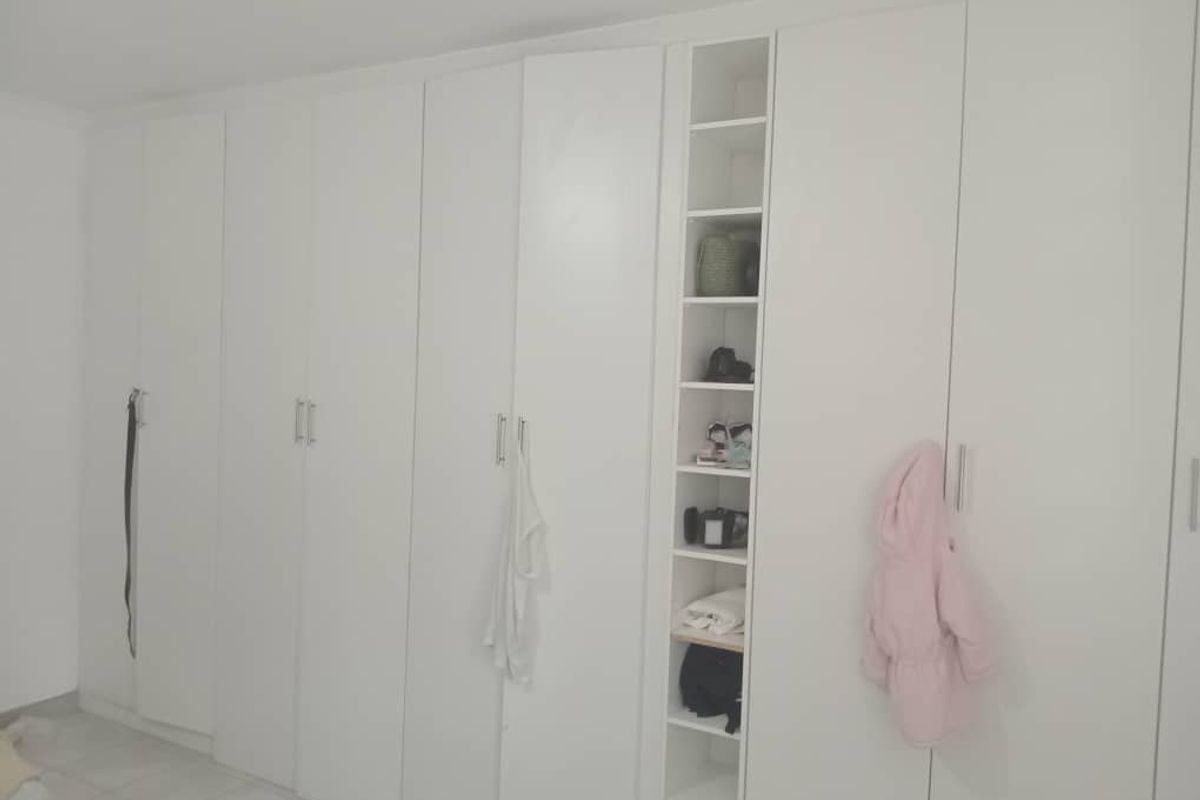 A bedroom featuring a large wall-to-wall built-in wardrobe with integrated shelving and white cabinetry.