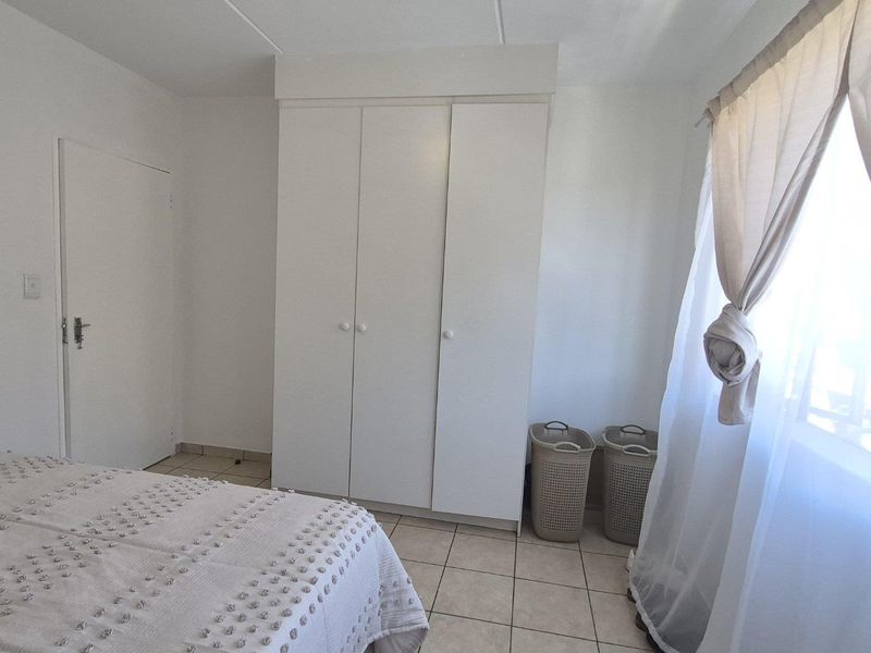 A bedroom featuring tiled flooring and a white built-in wardrobe, offering a clean and functional space.