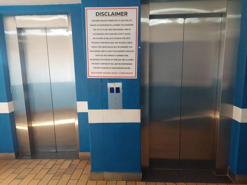 A communal elevator lobby area featuring two stainless steel lift doors and tiled flooring within an apartment building.