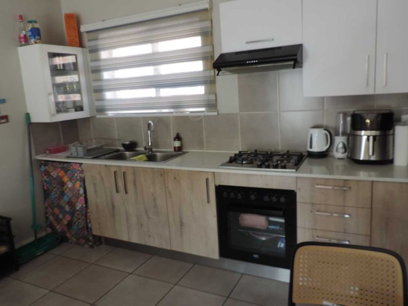 Functional kitchen featuring light wood-finish cabinetry, a gas hob, built-in oven, extractor fan, and tiled backsplash with neutral floor tiles.