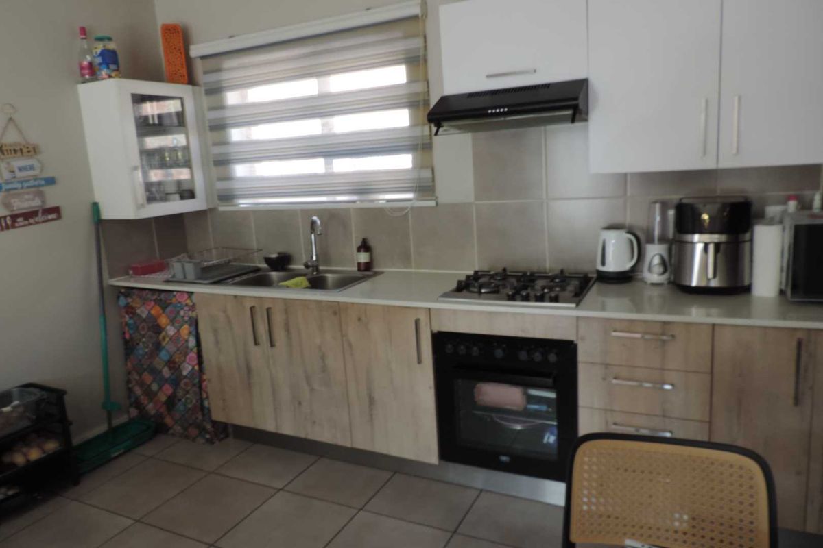 Functional kitchen featuring light wood-finish cabinetry, a gas hob, built-in oven, extractor fan, and tiled backsplash with neutral floor tiles.