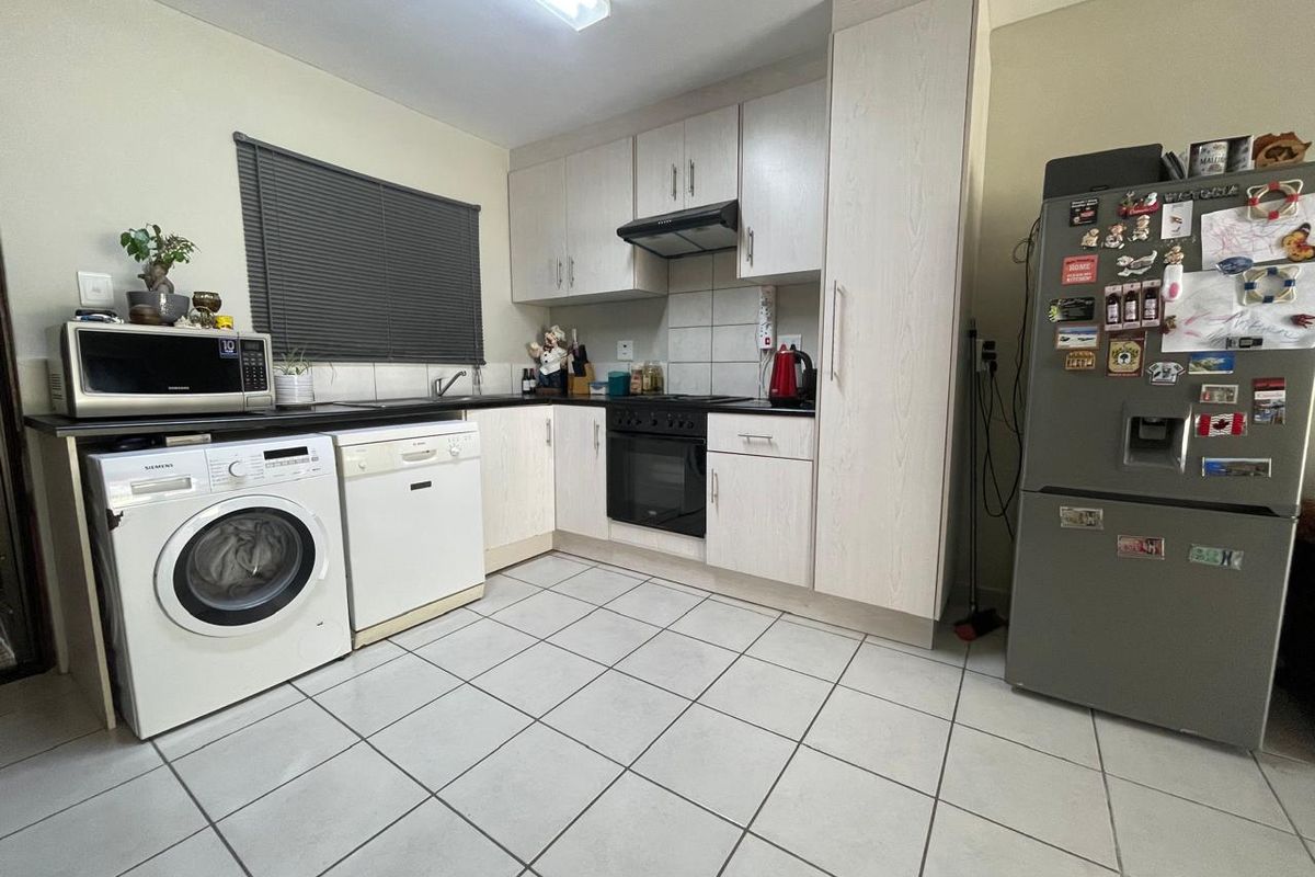 Functional kitchen featuring light-toned cabinetry, tiled flooring, built-in oven with extractor fan, and integrated space for laundry and dishwasher appliances.