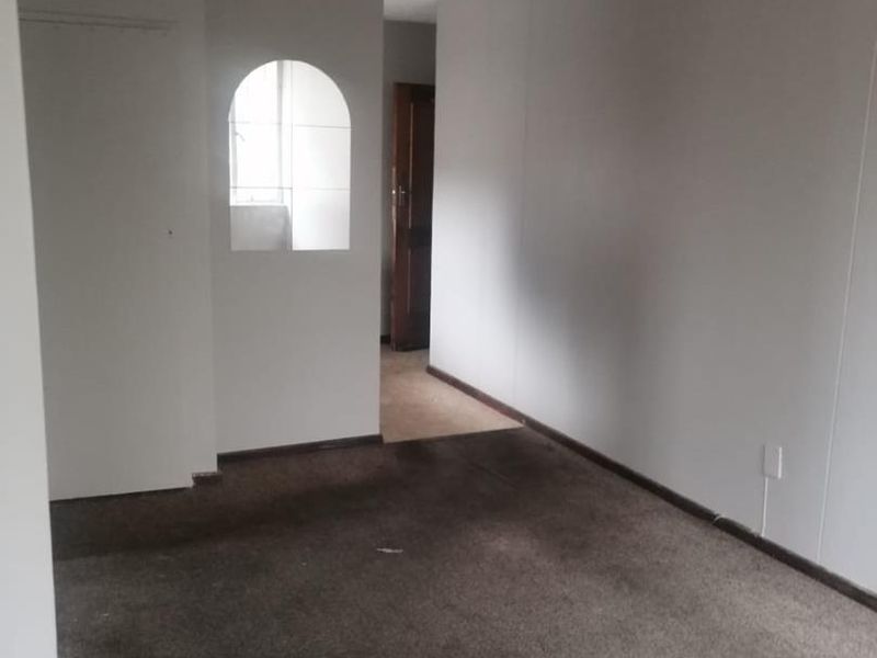 An empty living room featuring an arched wall opening and worn, stained carpeting, offering a blank canvas for renovation.