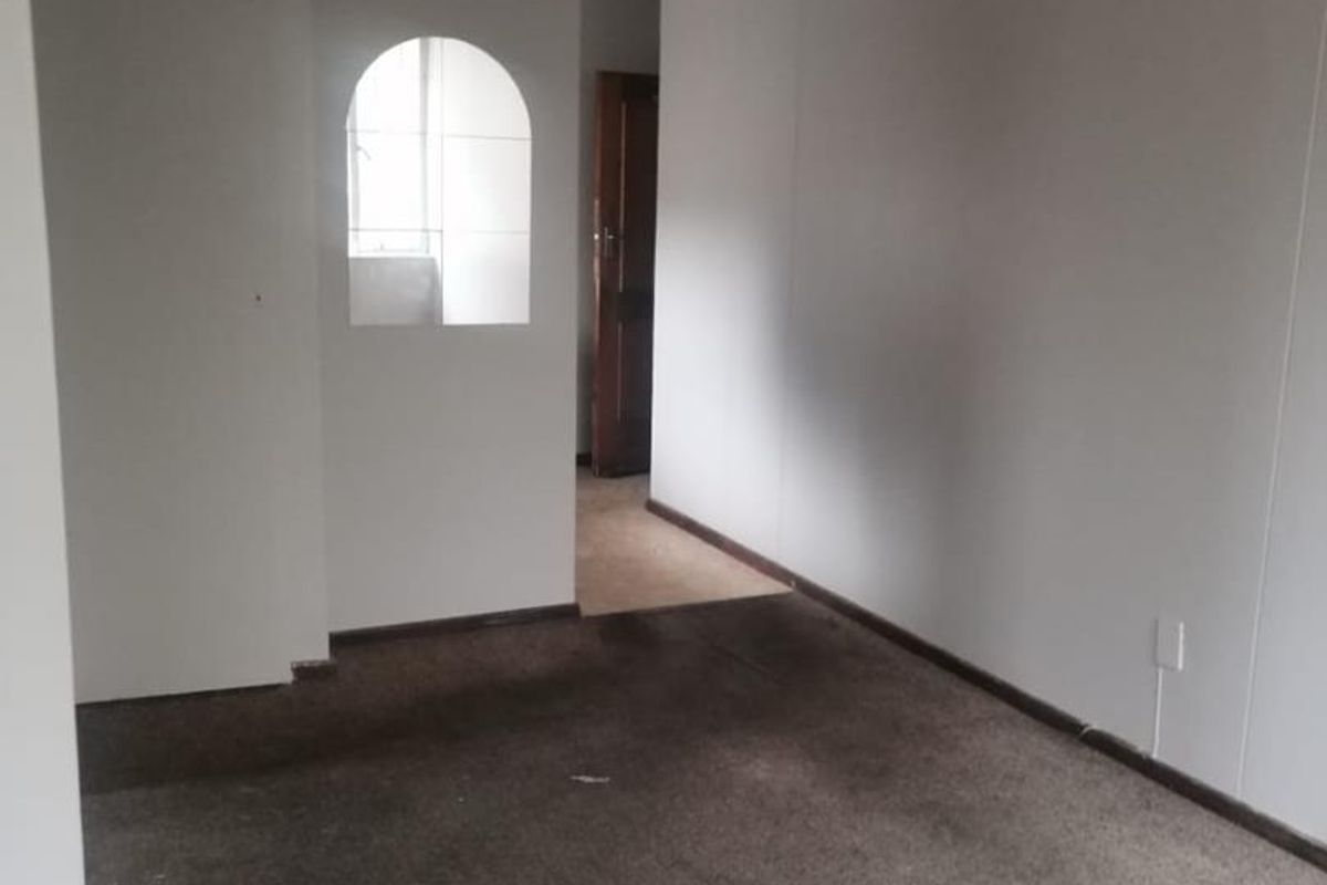 An empty living room featuring an arched wall opening and worn, stained carpeting, offering a blank canvas for renovation.