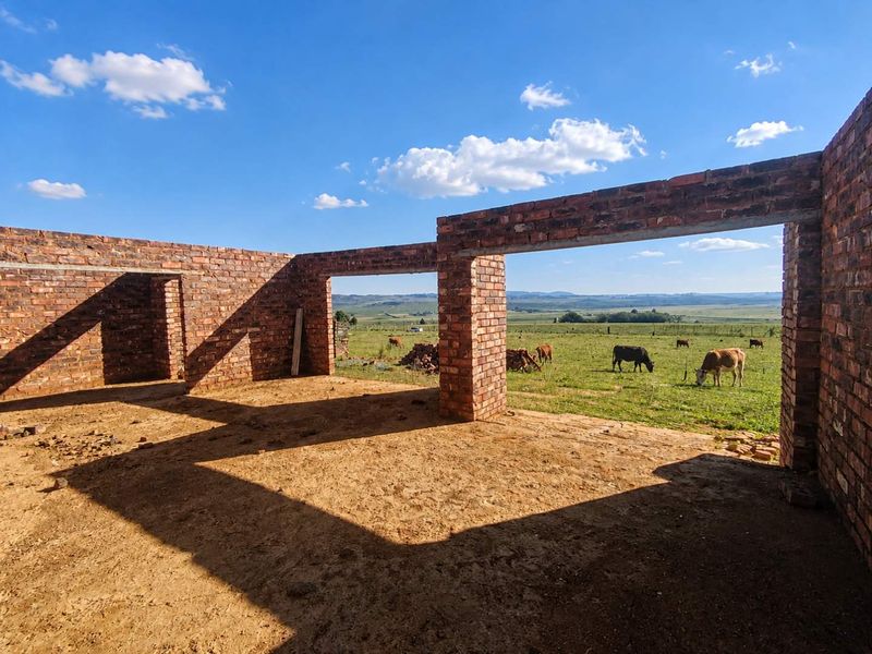 An unfinished brick structure under construction, featuring open wall frames and expansive views of the surrounding rural farmland.
