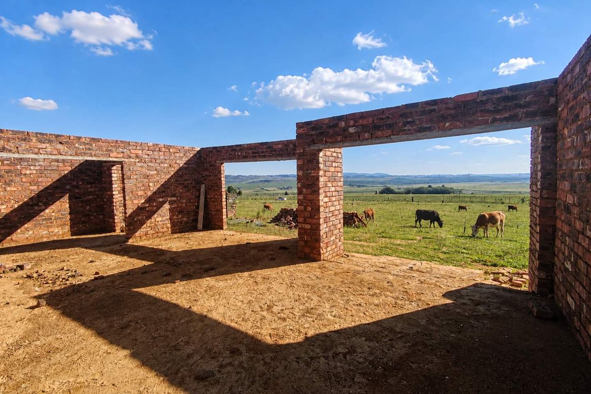 An unfinished brick structure under construction, featuring open wall frames and expansive views of the surrounding rural farmland.