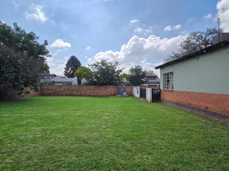 A spacious rear garden featuring a well-maintained lawn, enclosed by a brick boundary wall and side access gate.